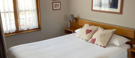 A neatly made bed in a hotel room with a wooden headboard, a nightstand with a lamp, and two framed pictures on the wall.