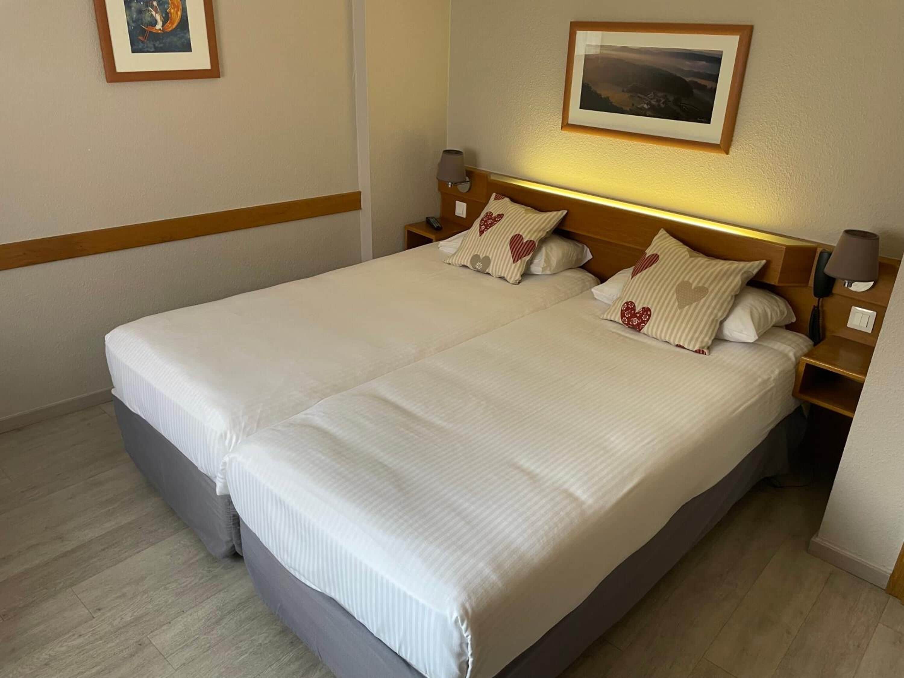 Una cama doble con sábanas blancas, dos mesitas de noche con lámparas y un cuadro enmarcado sobre la cama.