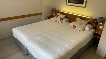 Una cama doble con sábanas blancas, dos mesitas de noche con lámparas y un cuadro enmarcado sobre la cama.