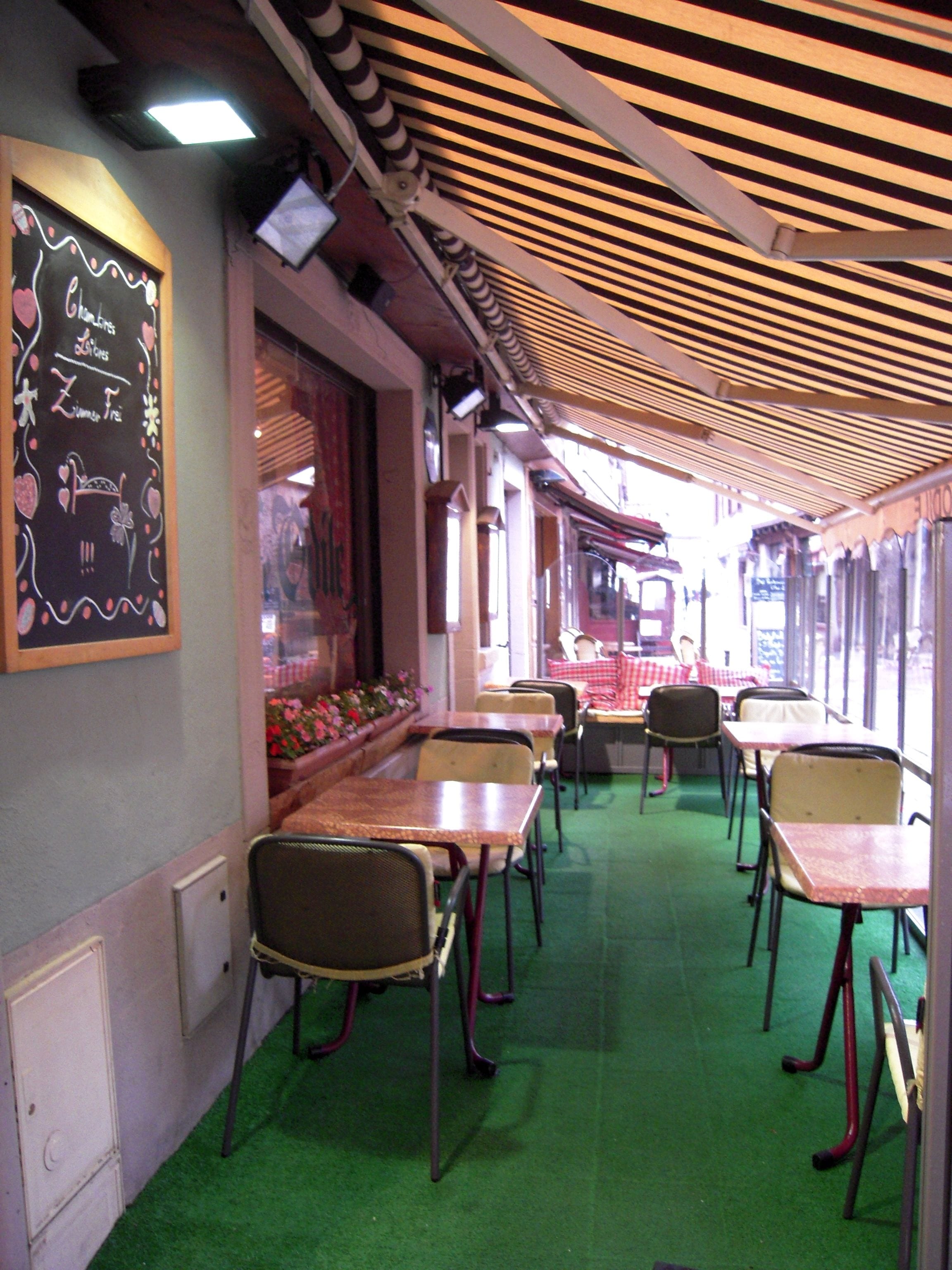 Interior de un restaurante con mesas y sillas, una alfombra verde y un menú en una pizarra en la pared.