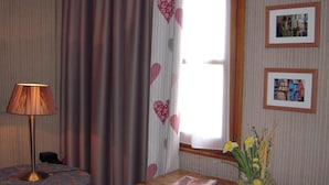A room with a wooden desk, a lamp, a window with heart-patterned curtains, and framed pictures on the wall. - Hôtel Sainte Odile (Obernai)