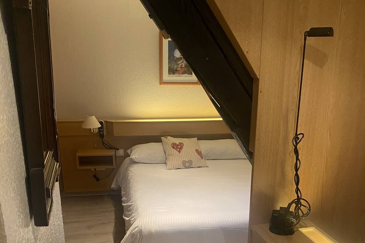 A bedroom with a bed, bedside table, lamp, and a painting on the wall.