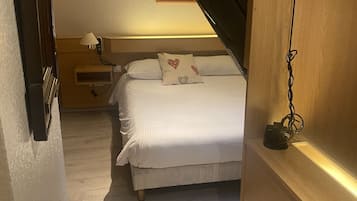 Un dormitorio con cama, mesita de noche, lámpara y un cuadro en la pared.