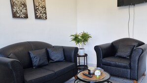 Un salon moderne avec un canapé en cuir noir, une table basse ronde et un tapis à rayures. Deux tableaux sont accrochés au mur, et une plante en pot est posée sur le sol.