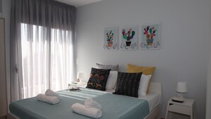 A neatly made bed with rolled towels, a bedside table with a lamp, and three cactus-themed wall art pieces. - Edem apartment Sea View (Palaio Faliro)
