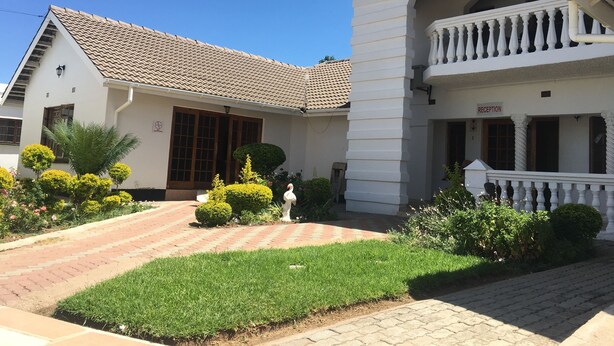 A building with a tiled roof, a reception area, and a well-maintained garden with hedges and a lawn. - Tashatha Hotel (Tutume)