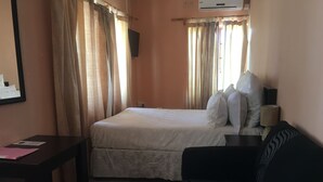 A hotel room with a bed, a desk, a chair, a lamp, and a TV. - Tashatha Hotel (Tutume)