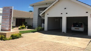 A building with a sign indicating directions to various rooms and amenities, a parking area, and a car parked in the garage. - Tashatha Hotel (Tutume)