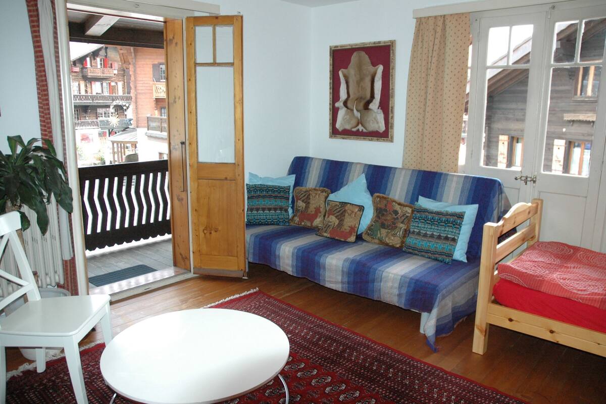 A cozy room with a sofa, a wooden chair, a small table, and a red rug.