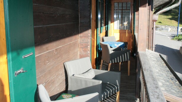 Fachada de madera con un porche cubierto, dos sillas, una mesa y vista a la calle.