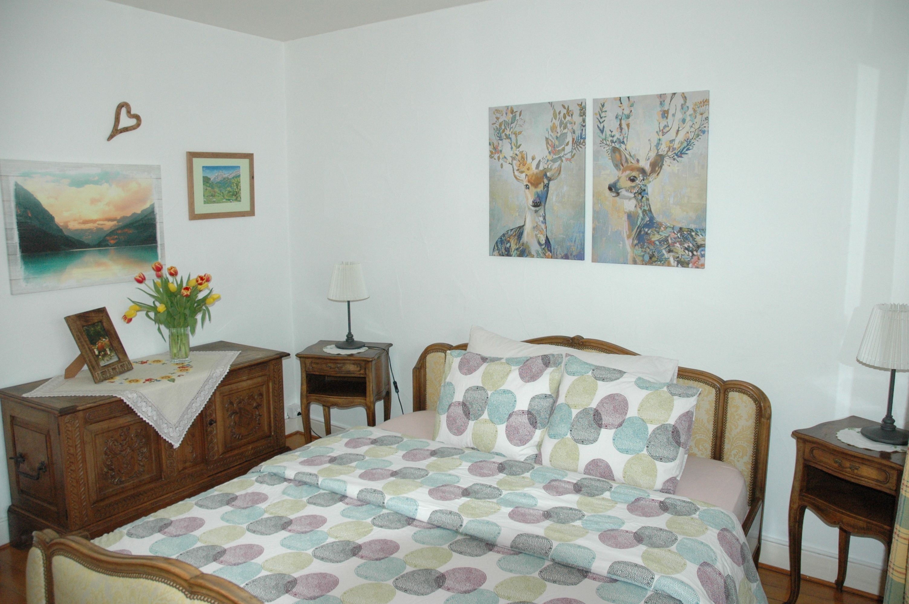 Un dormitorio con cama, mesita de noche, cómoda y una pared con dos cuadros.