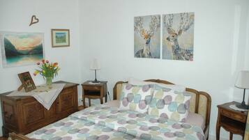 Un dormitorio con cama, mesita de noche, cómoda y una pared con dos cuadros.