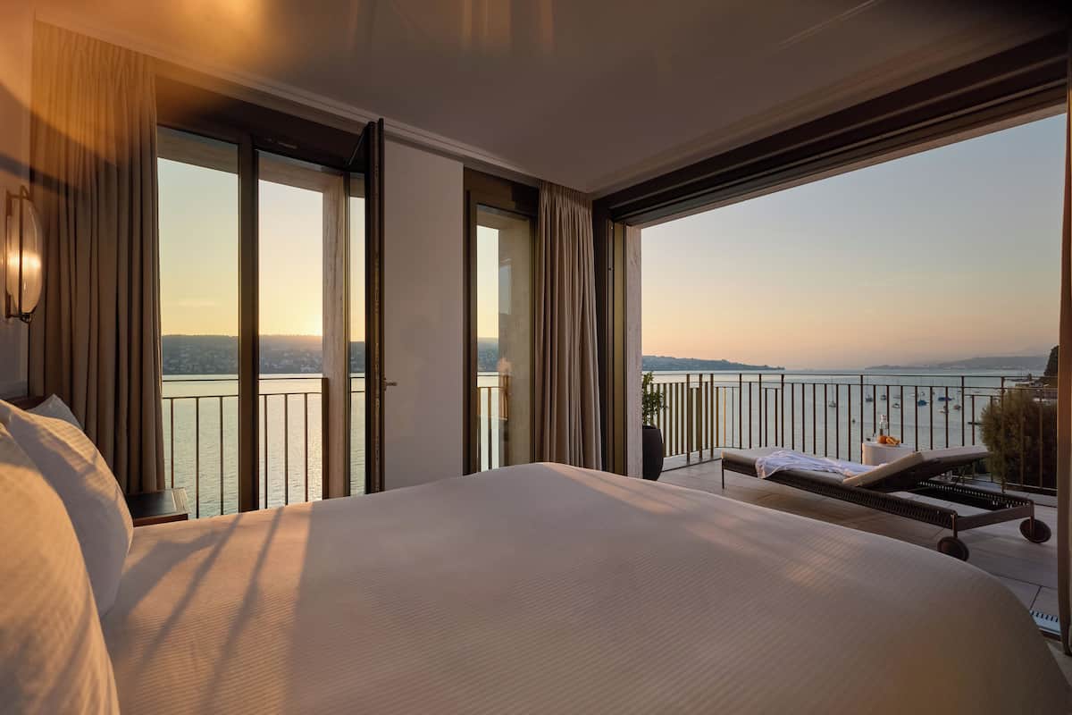 Ett hotellrum med en stor säng, en balkong med utsikt över havet och en lounge med en solstol.