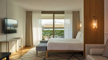 A hotel room with a bed, a TV, a sofa, a small table, and a window with curtains.