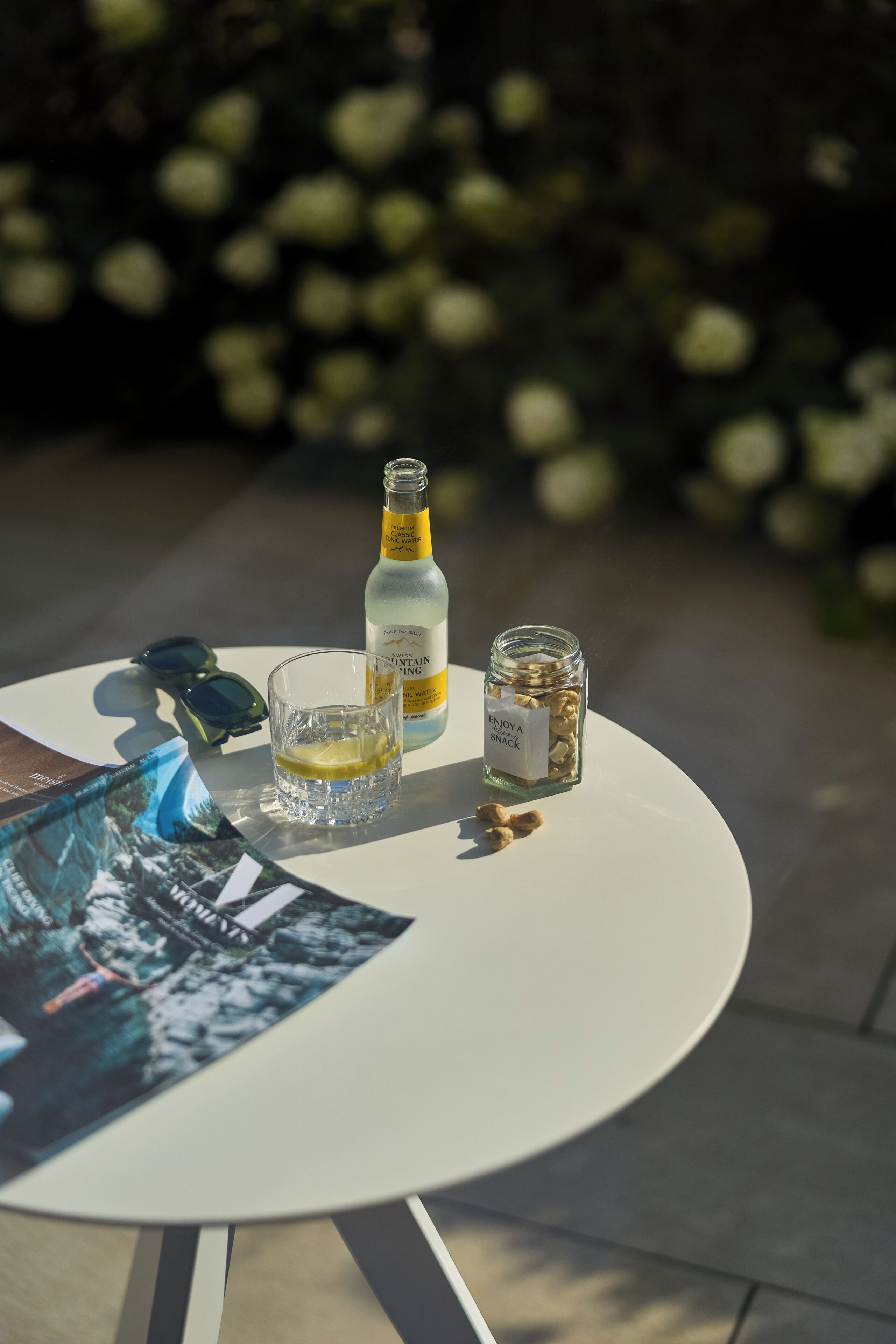 Ein runder Tisch mit einer Flasche, einem Glas und einer Dose Nüsse.
