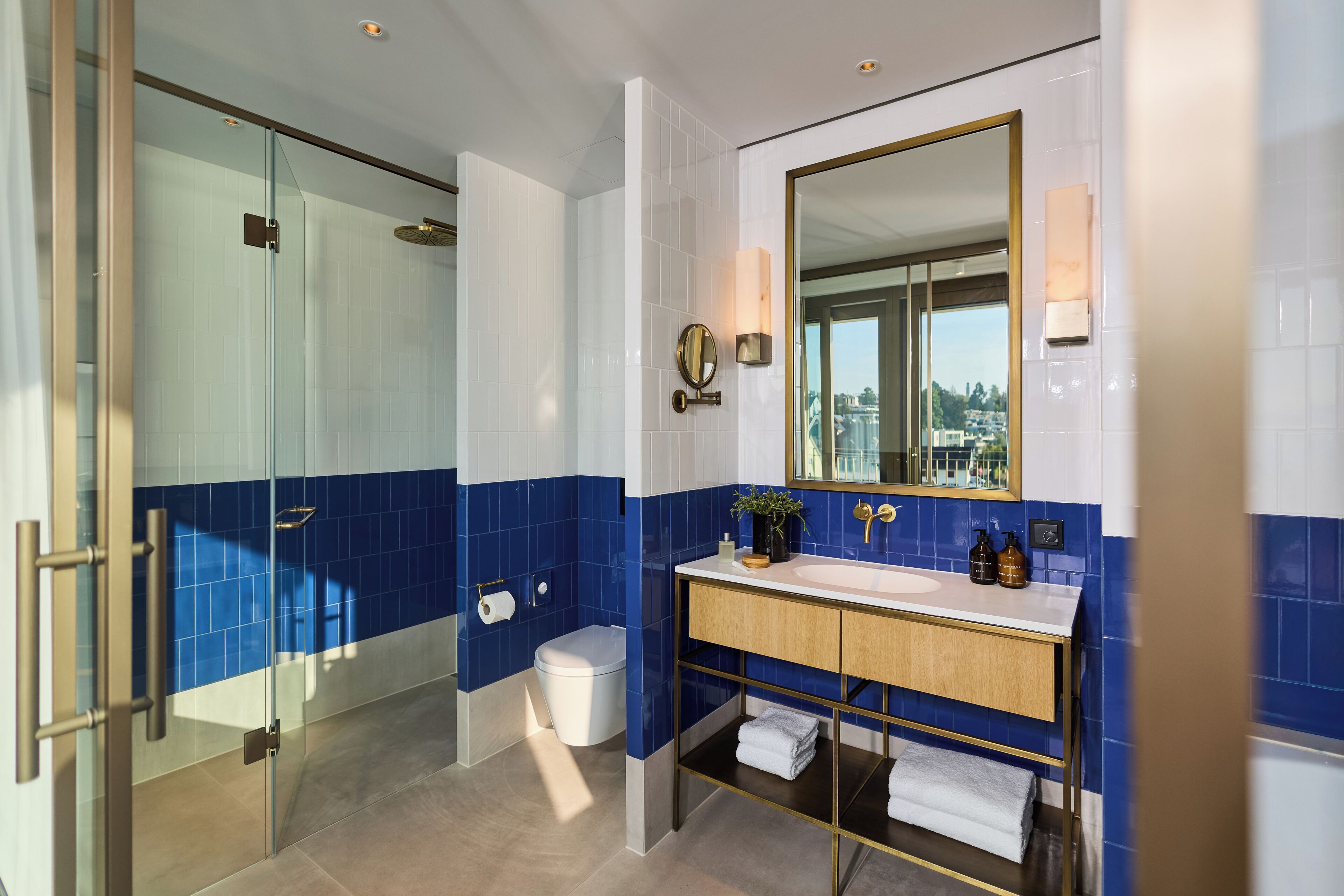 Un baño moderno con cabina de ducha de vidrio, inodoro blanco, lavamanos con espejo y toallero.