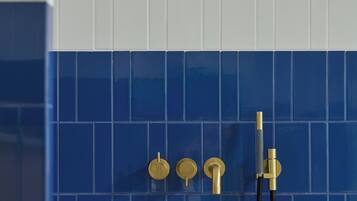 A bathroom with a blue-tiled wall, a white bathtub, and a gold faucet.