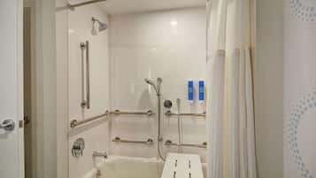 Un baño con ducha a nivel, barras de apoyo, un lavabo blanco y una bañera blanca.