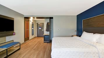 A hotel room with a large bed, a TV mounted on the wall, a bench, and a mirror.