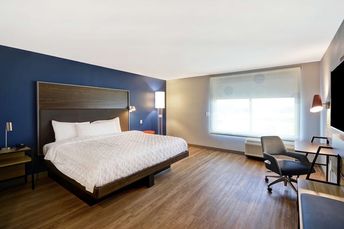 Una habitación de hotel con una cama grande, un escritorio, una silla y un ventanal amplio.