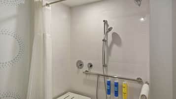 Une douche avec une porte en verre, un pommeau de douche amovible et deux bouteilles de shampoing et d’après-shampoing.