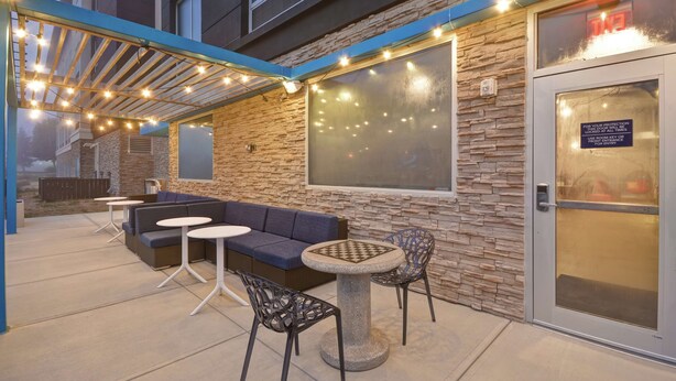 Een terras buiten met een stenen muur, een blauwe bank, twee witte tafels en twee stoelen.