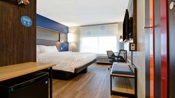 Une chambre d’hôtel équipée d’un lit, d’un bureau, d’une chaise et d’un téléviseur fixé au mur.
