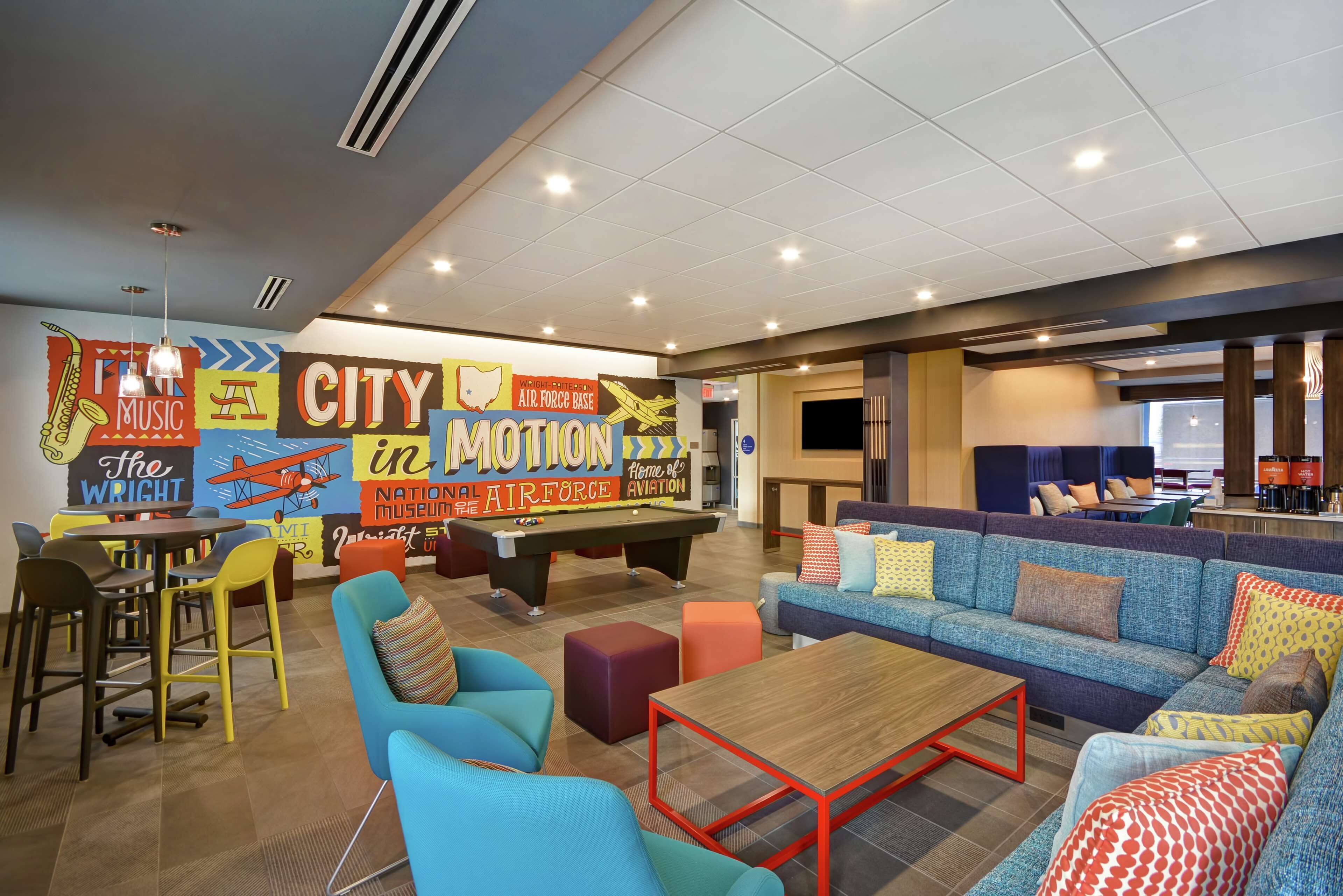 A vibrant lounge area with colorful seating, a pool table, and a mural depicting an air force base.