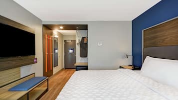 A hotel room with a large bed, a bench, a TV, and a desk with a lamp.