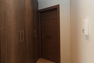 A closed wooden door with a handle and a lock, a white wall-mounted thermostat, and a tiled floor.