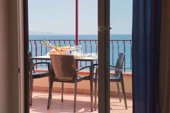 A balcony with a table set for two, overlooking a body of water. - La Sirena Bed & Breakfast (Santa Teresa di Riva)
