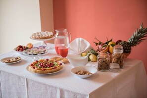 A table with various food items, including a fruit platter, pastries, and a pitcher of juice. - La Sirena Bed & Breakfast (Santa Teresa di Riva)