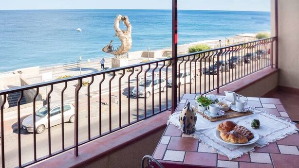 A balcony with a view of the sea, a table with breakfast items, and a decorative sculpture. - La Sirena Bed & Breakfast (Santa Teresa di Riva)