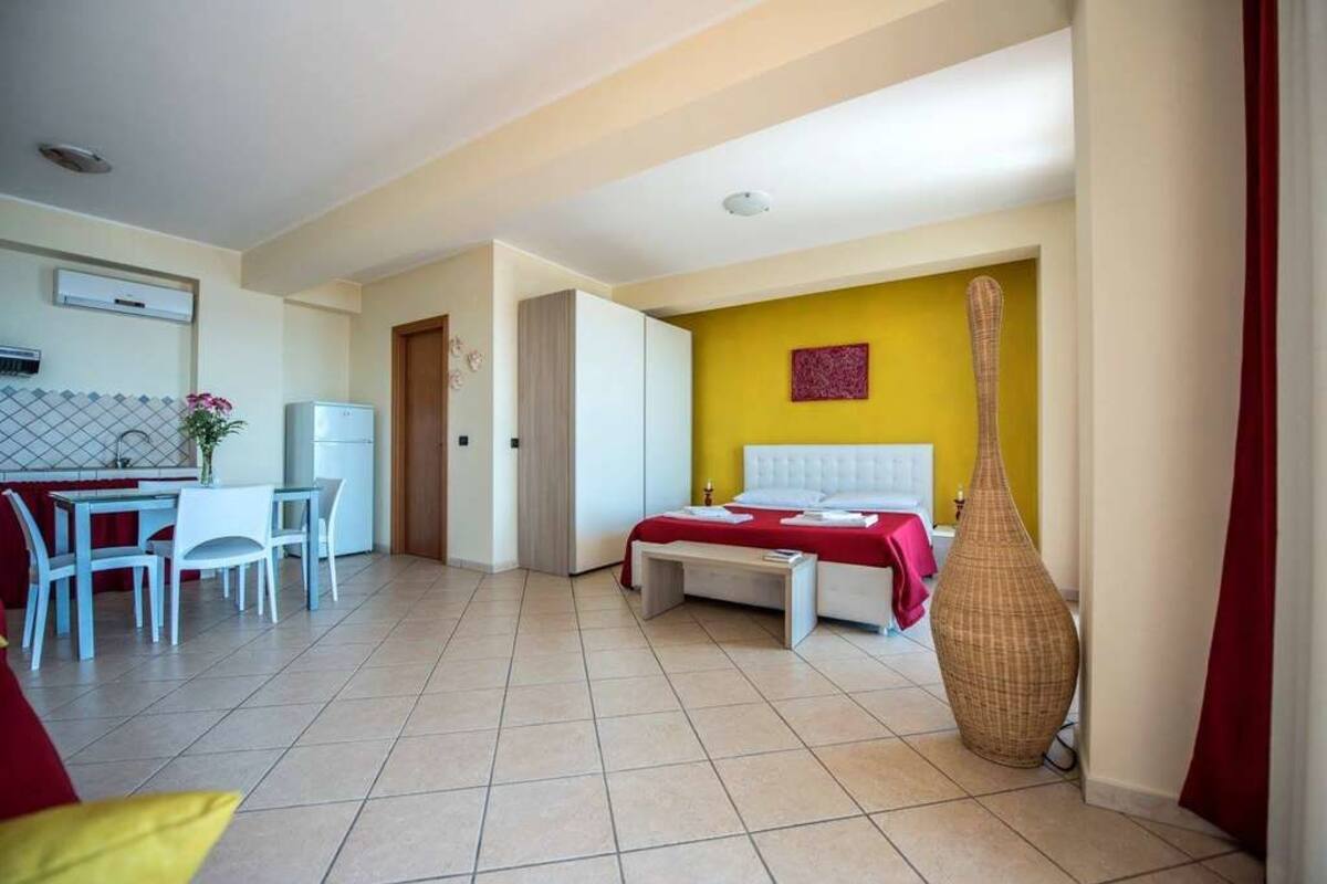 A hotel room with a bed, a dining area with a table and chairs, and a kitchenette.