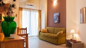 A living room with a sofa, a dining table with chairs, a green vase, and a painting on the wall. - La Sirena Bed & Breakfast (Santa Teresa di Riva)