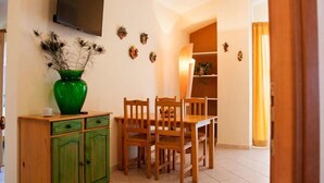 A dining area with a wooden table and chairs, a green cabinet, and a flat-screen TV mounted on the wall. - La Sirena Bed & Breakfast (Santa Teresa di Riva)