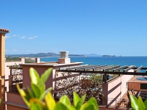 A rooftop terrace with a pergola, a hot tub, and a view of the sea and distant hills.