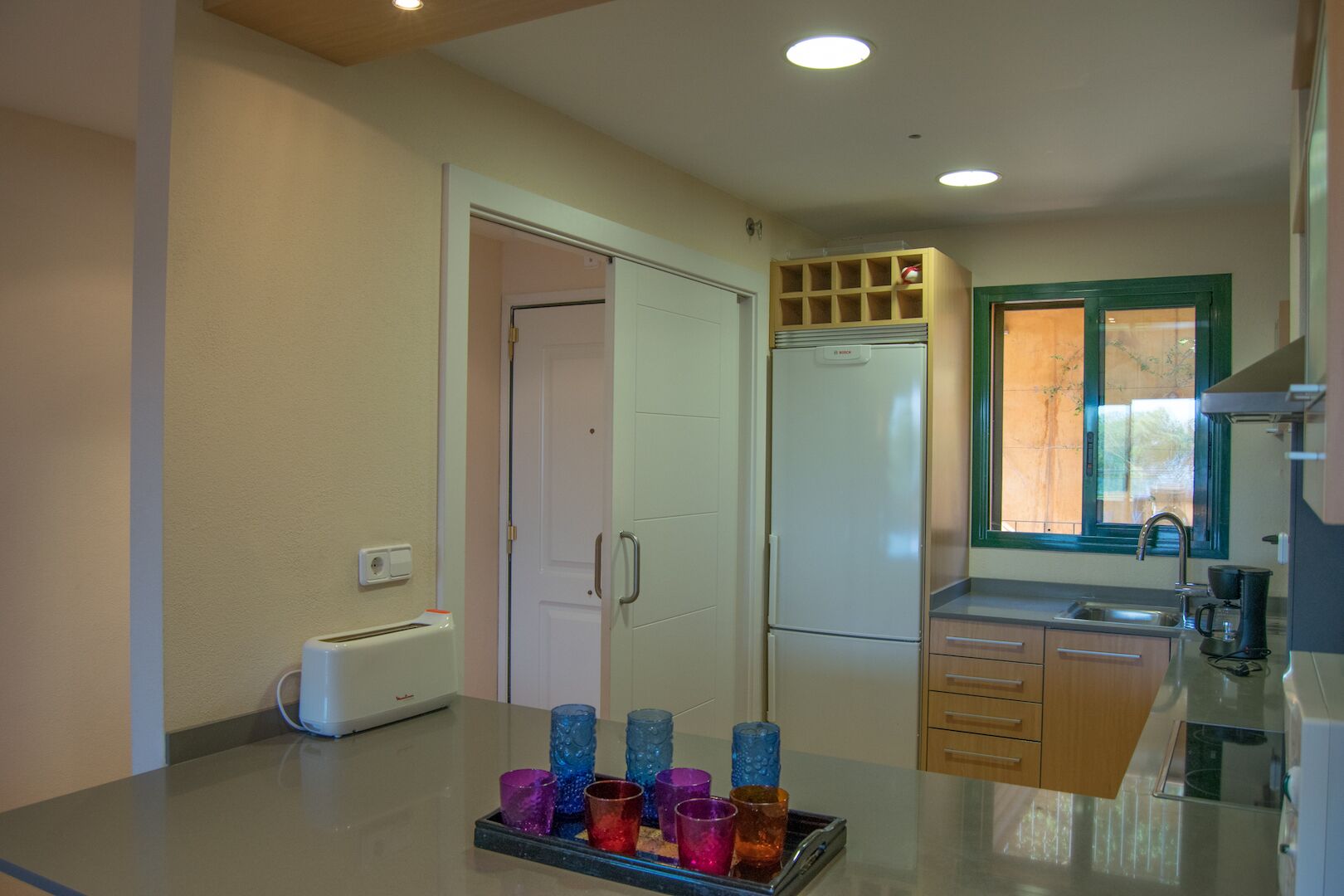 A modern kitchen with a refrigerator, a coffee maker, and a window with a view.