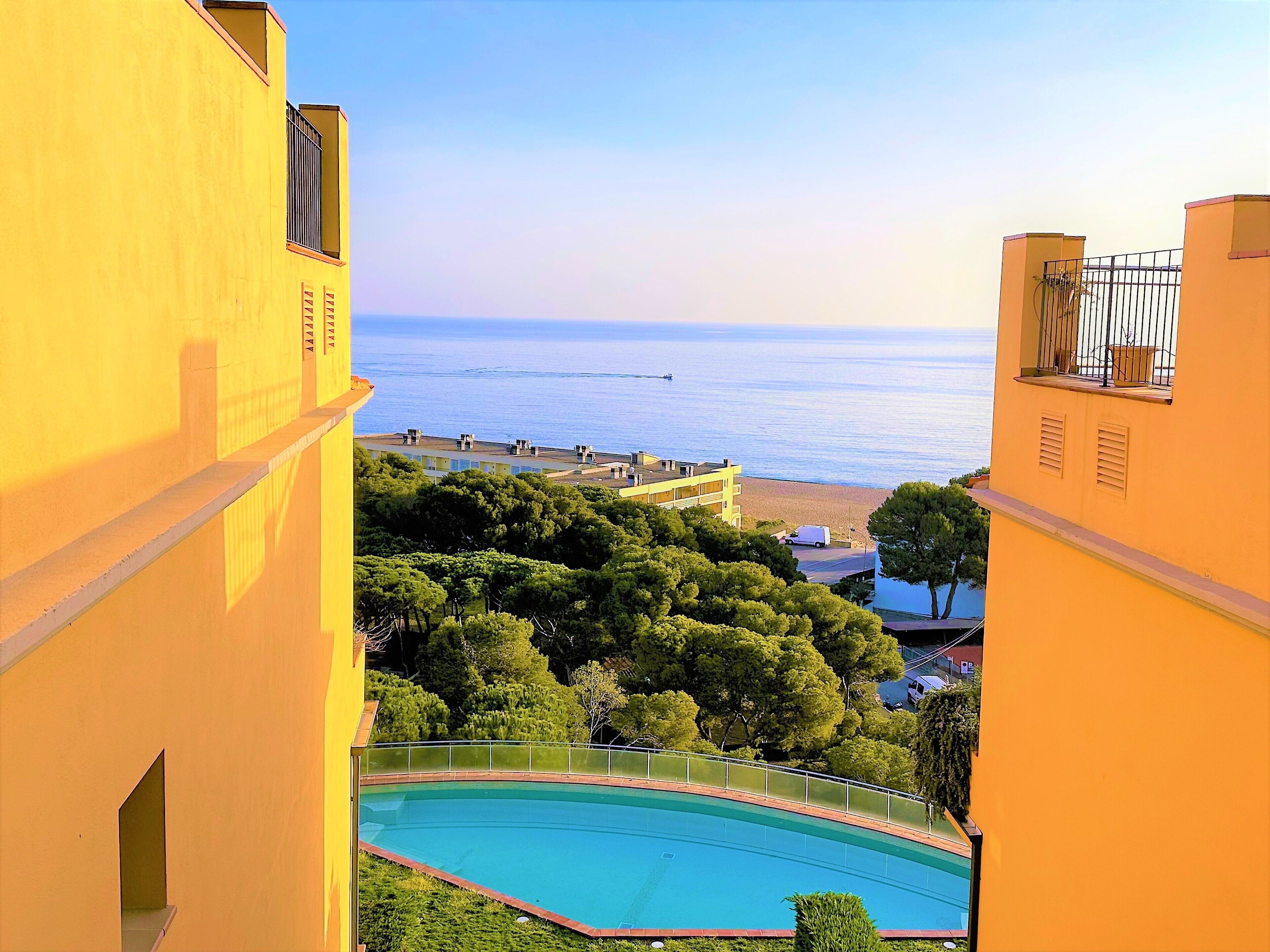 Un edificio amarillo con piscina, árboles y vistas al mar.