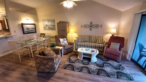 Ein Wohnzimmer mit einem Glastisch, zwei Sesseln, einem Sofa, einem gemusterten Teppich und einem Wandbild.