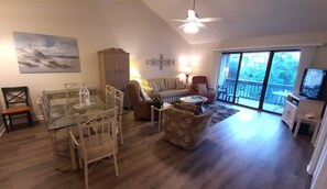 A spacious living room with a glass dining table, a sofa, a chair, and a television.