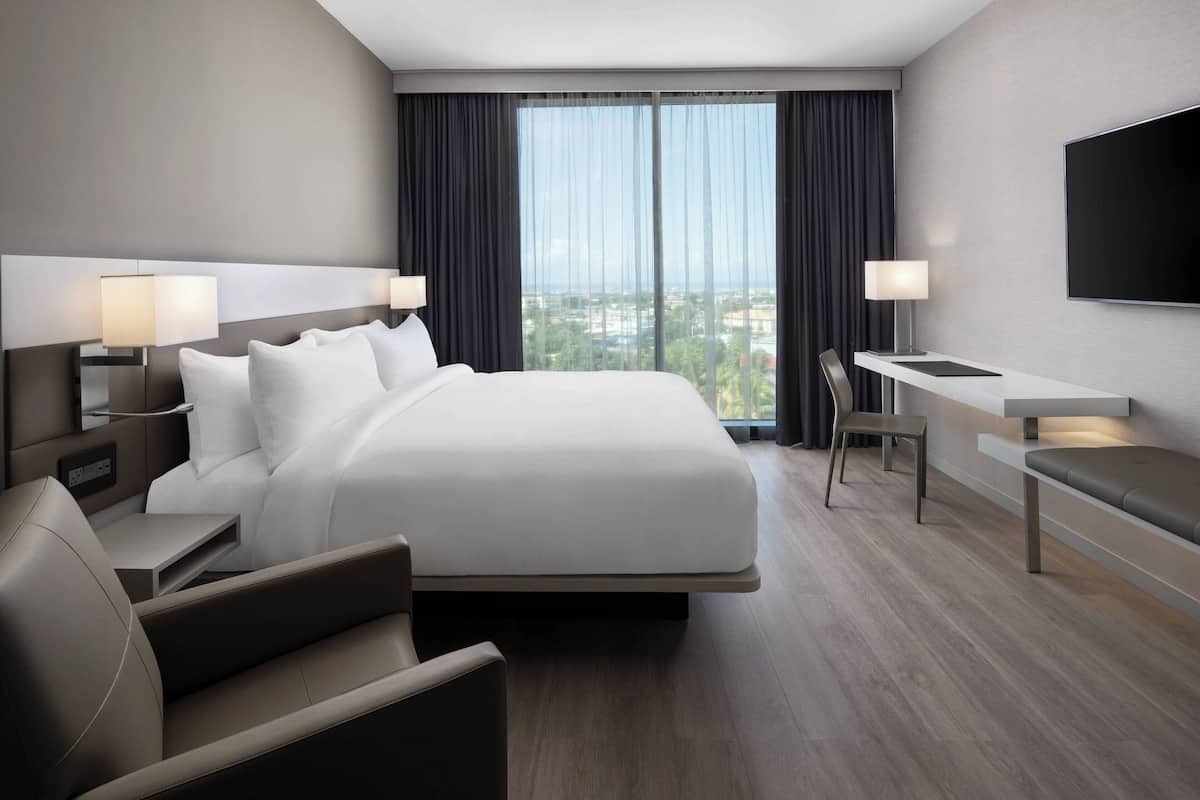 Une chambre d’hôtel moderne dotée d’un grand lit, de tables de chevet avec des lampes, d’un bureau et d’un téléviseur fixé au mur.