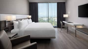 A modern hotel room with a large bed, bedside tables with lamps, a desk, and a TV mounted on the wall.