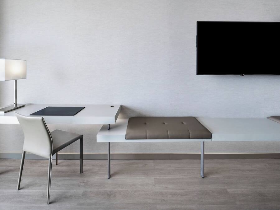 A modern room with a desk, chair, bench, and a flat-screen TV mounted on the wall.