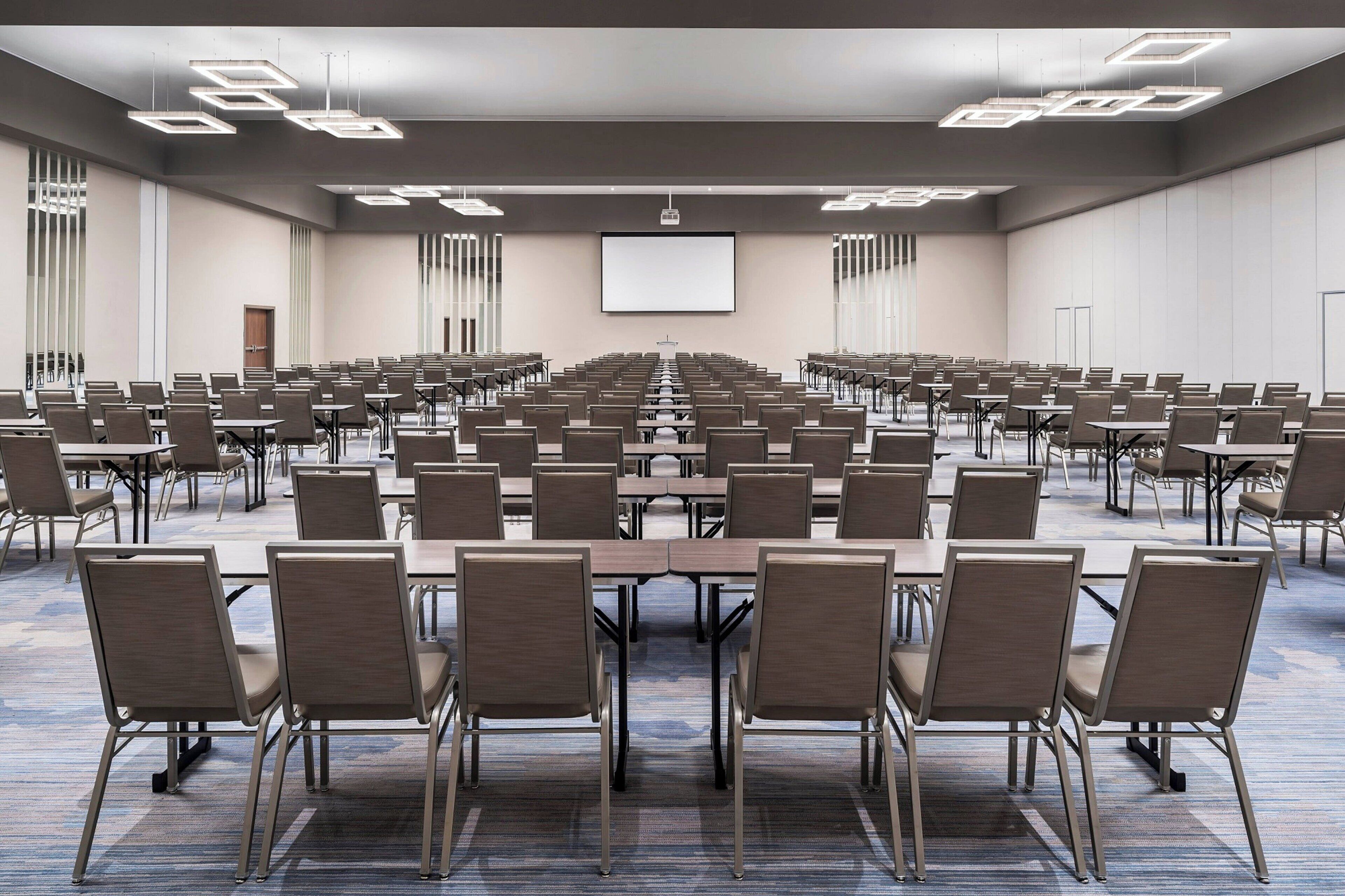 A large conference room with rows of tables and chairs, a projector screen, and a carpeted floor.