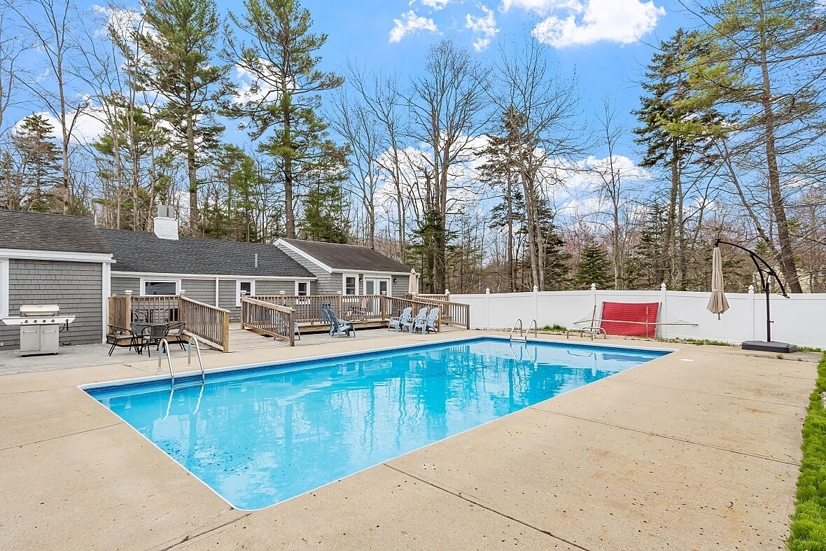 Une piscine rectangulaire dotée d’une terrasse en bois et de chaises longues.