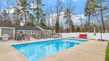 Une piscine rectangulaire dotée d’une terrasse en bois et de chaises longues.