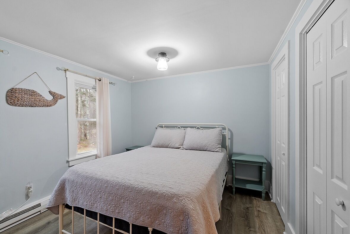 A bedroom with a bed, a bedside table, a hanging basket, and a window with curtains.