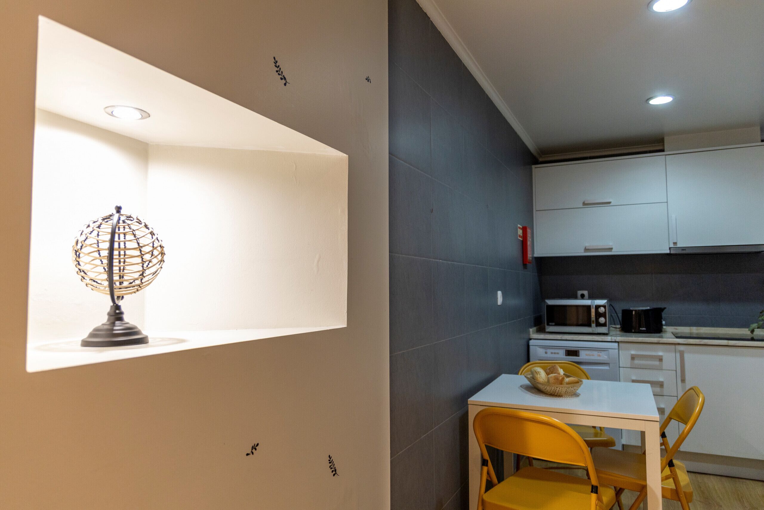 Una cocina con gabinetes blancos, un microondas, un lavamanos y una mesa de comedor con sillas amarillas.