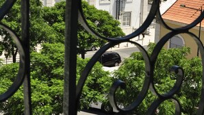 Une vue à travers une structure métallique ouvragée, représentant une rue bordée de voitures garées, d’arbres et d’immeubles aux toits recouverts de tuiles rouges.